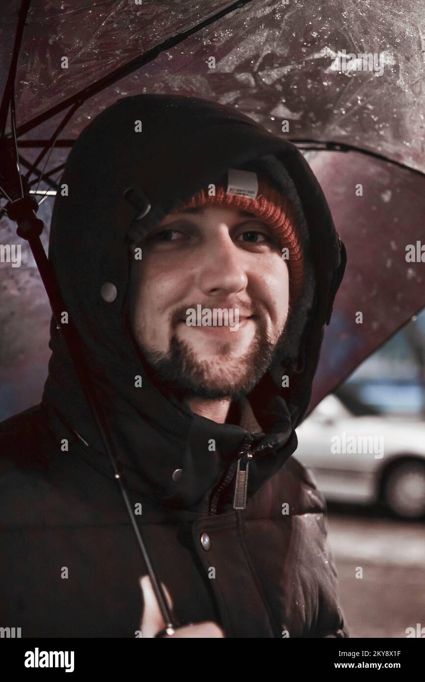 Young happy man under umbrella looking at camera smiling. Bad weather Stock Photo