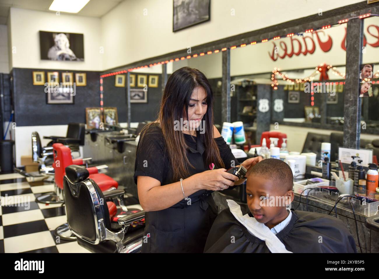Woman Barber and hairstylist Cutting a young black boy’s hair Stock Photo