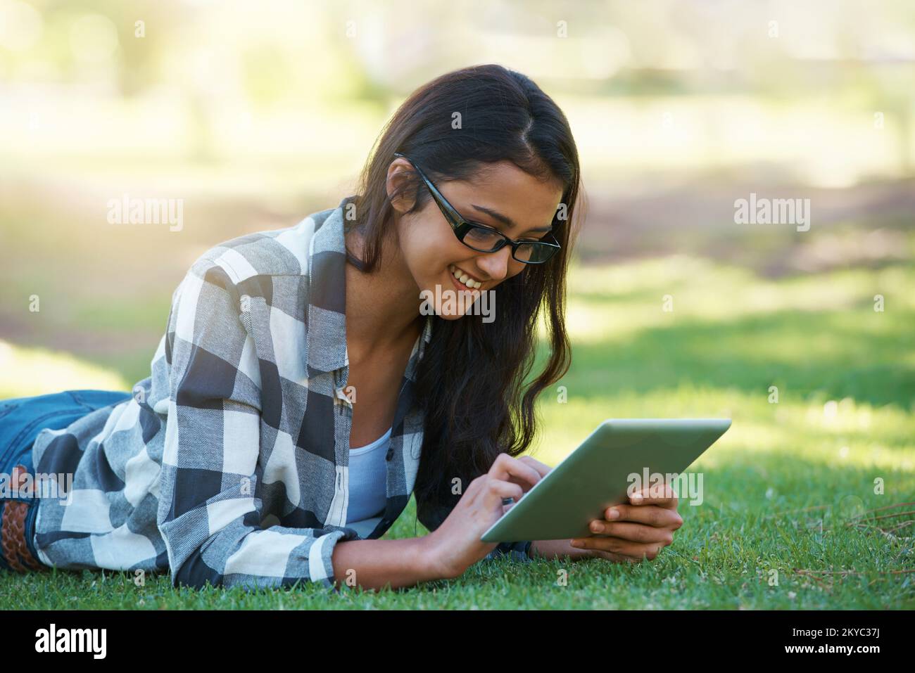 Staying connected wherever I go. A young woman working on a touchpad while lying ijn a park. Stock Photo