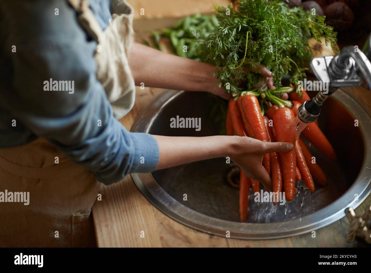 Washing them off before its time to cook. a woman washing carrots in a sink. Stock Photo