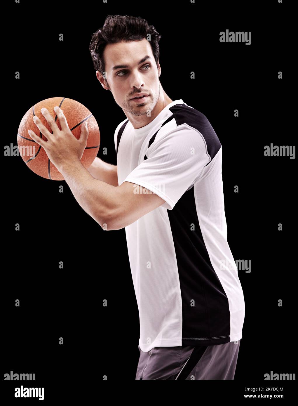 Shooting hoops. A young man about to throw a basketball against a black