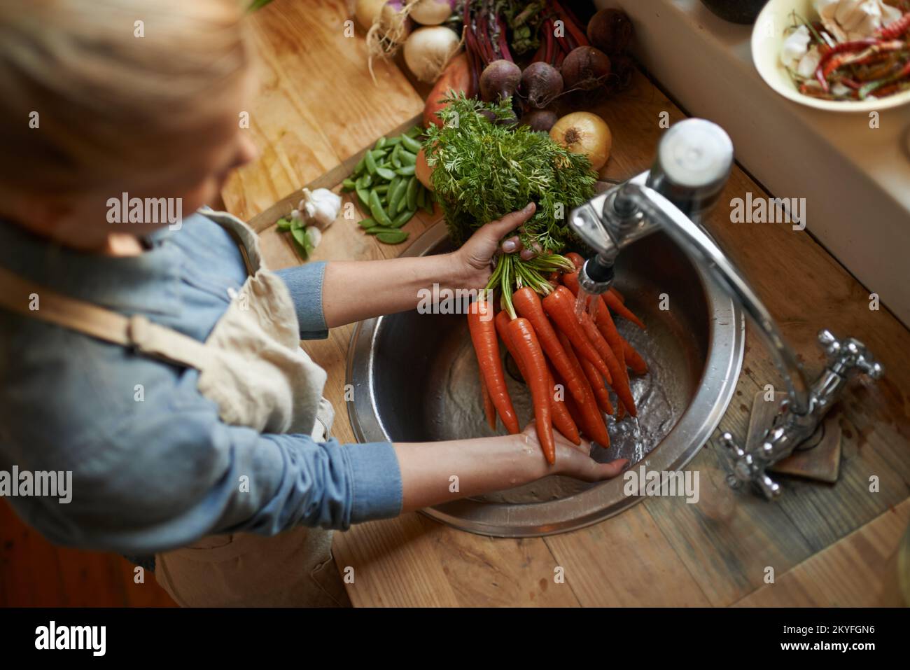 Washing them off before its time to cook. High angle shot of a woman washing carrots in a sink. Stock Photo