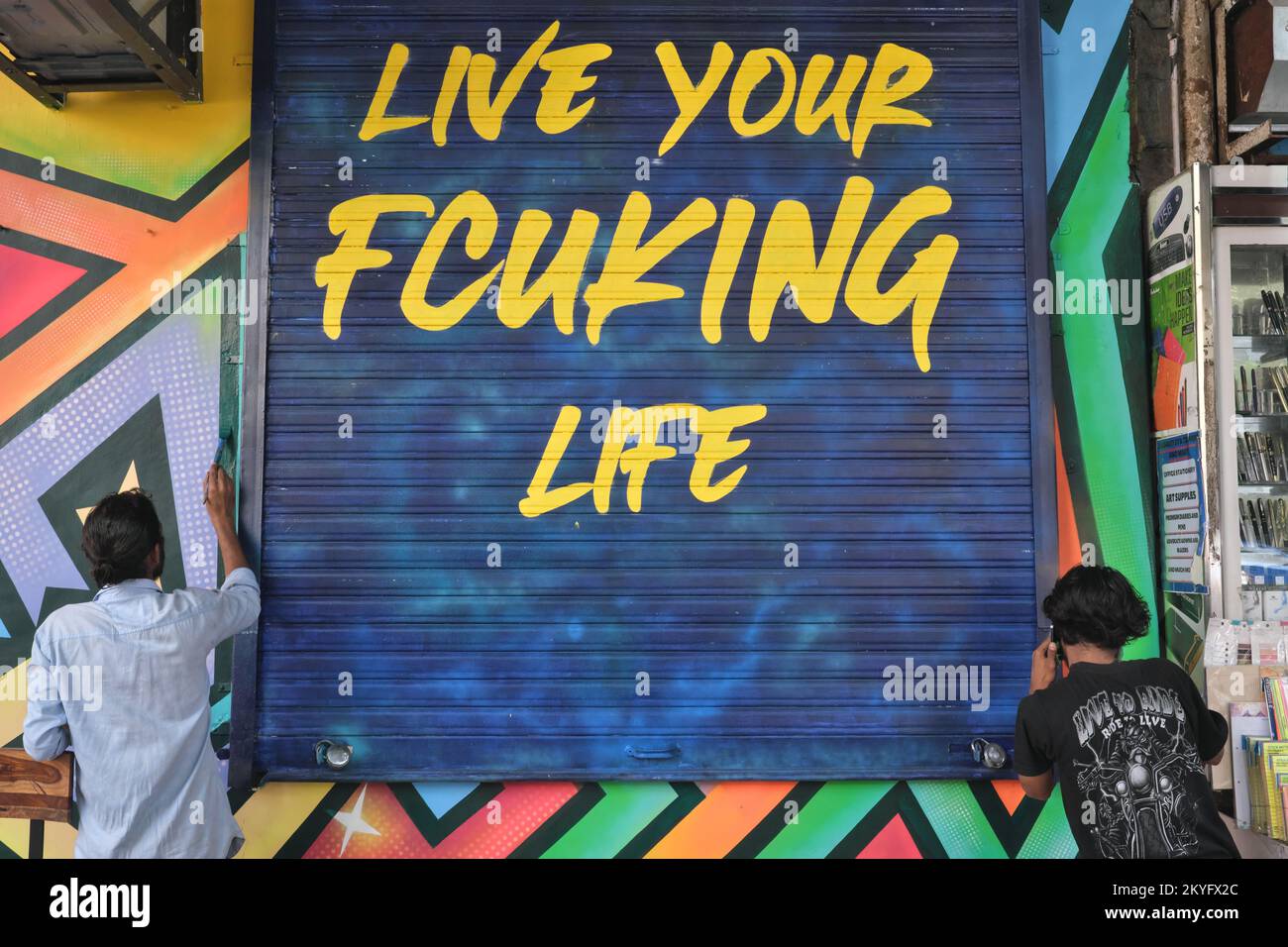 Workers in Mumbai, India, painting a shop entrance, including the slogan Live Your Fcukin Life on the door shutters Stock Photo