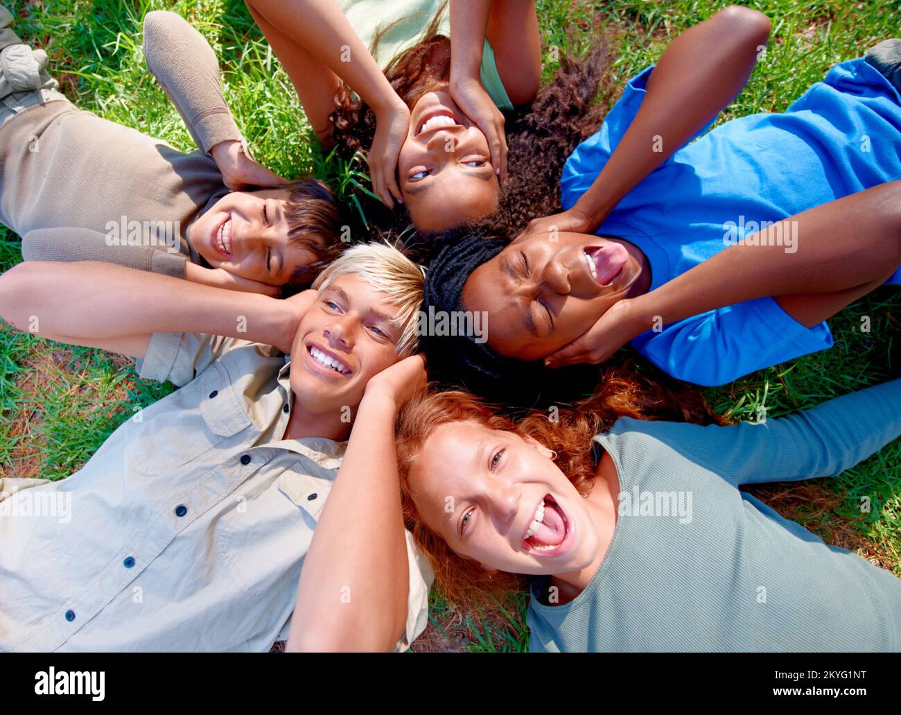 We cant contain the joy. High angle view of a group of kids lying down and covering their ears while they laugh at the camera. Stock Photo