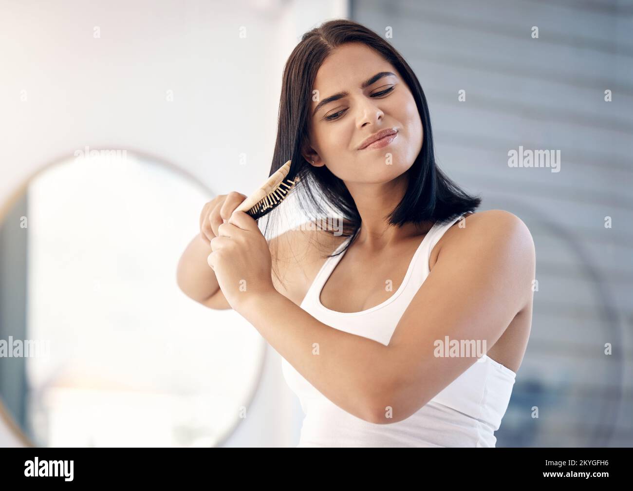 Hair, brush and split ends with a woman in the bathroom of her home, brushing her knots for grooming. Stress, beauty and haircare with a frustrated Stock Photo