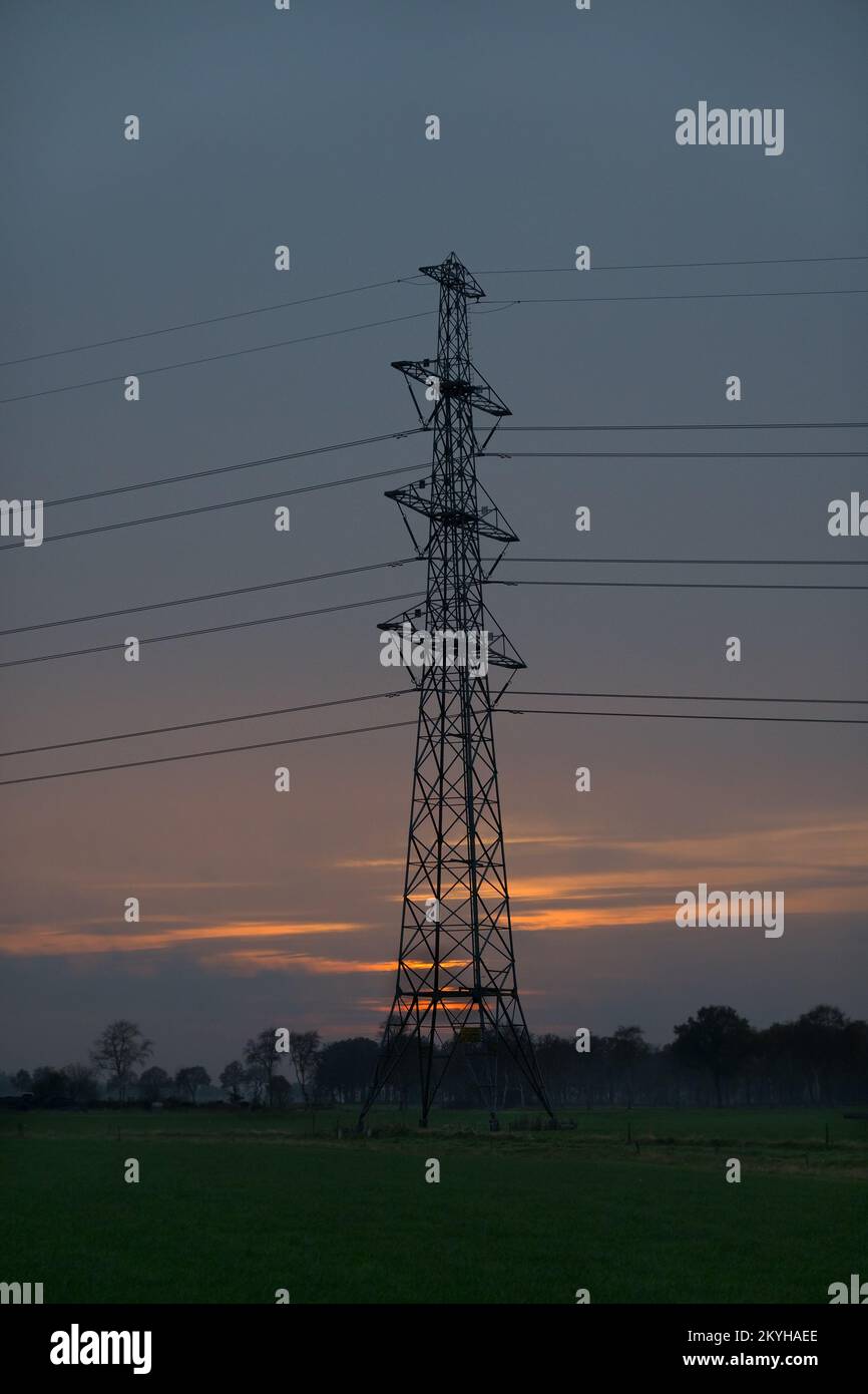 Silhouette of electricity pylon with wires against sunset sky Stock Photo