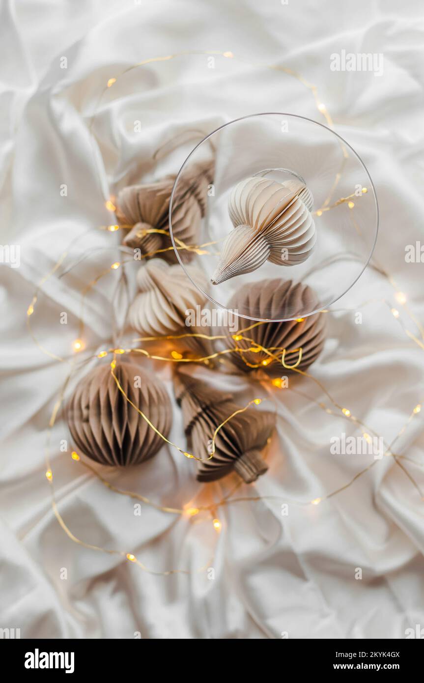 Christmas toys made of paper on a silk sheet, wineglass and lights. Stock Photo