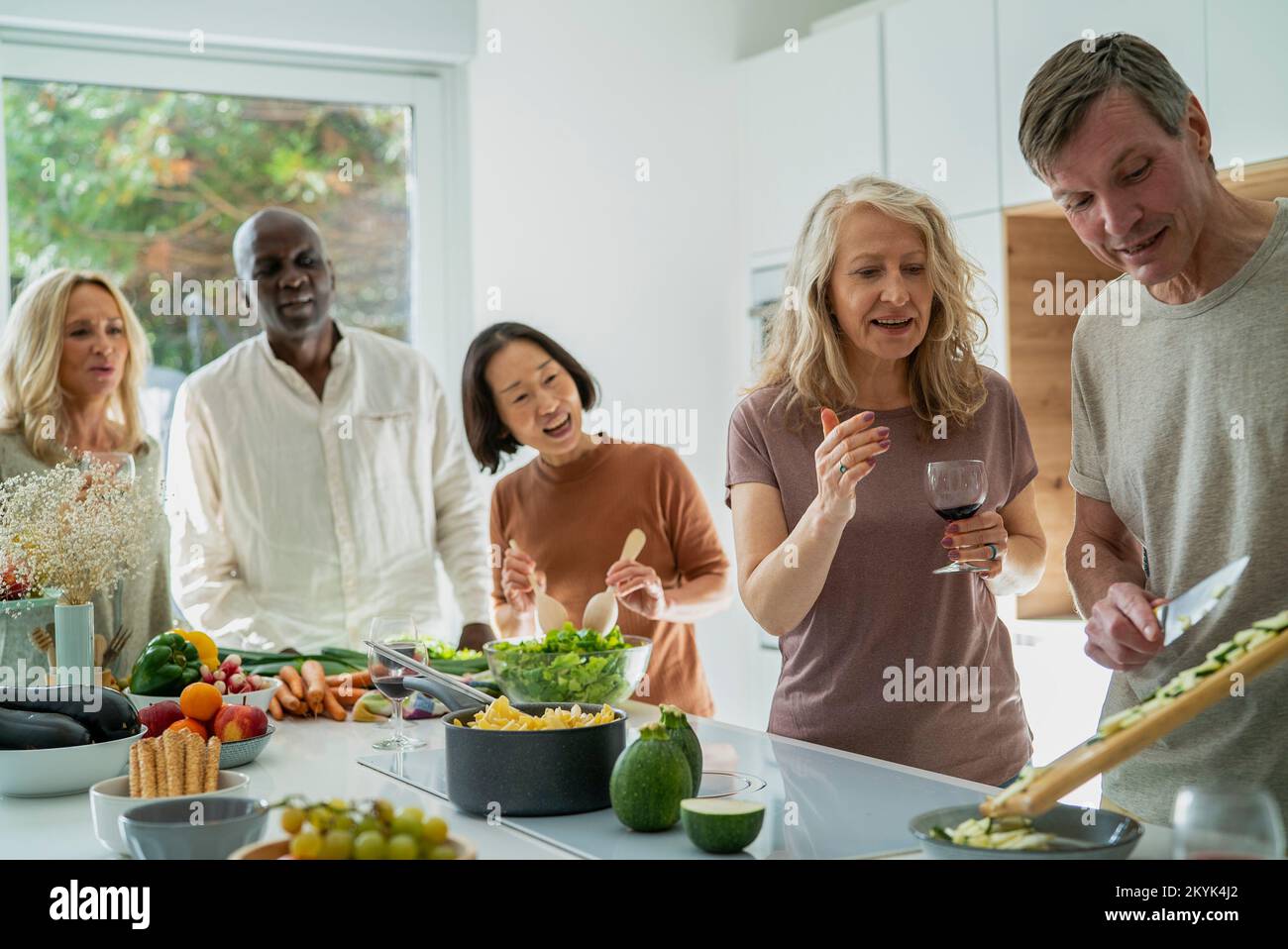 Diverse group of senior friends gathered at kitchen while cooking Stock Photo