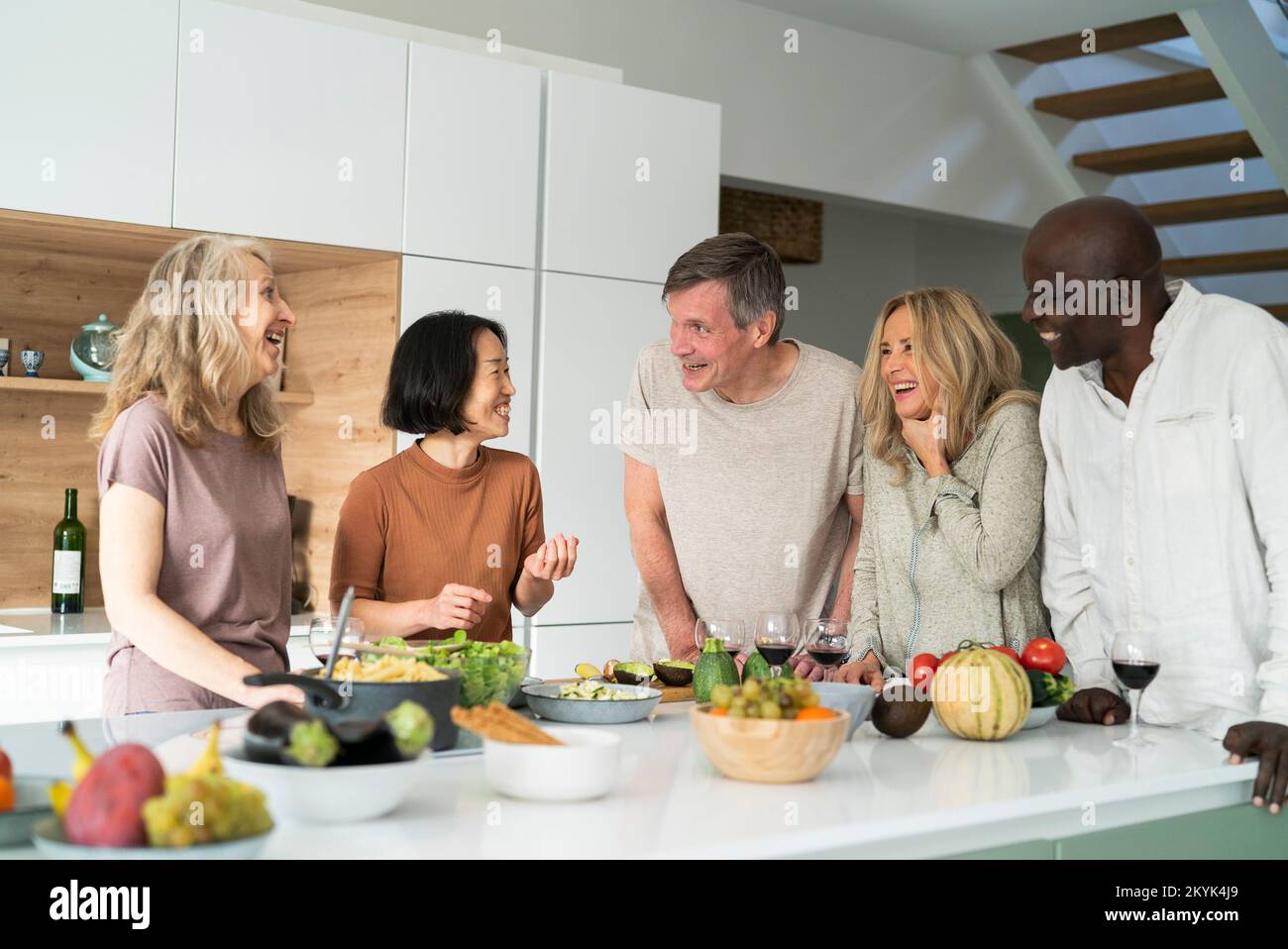 Diverse group of senior friends gathered at kitchen counter while drinking wine Stock Photo