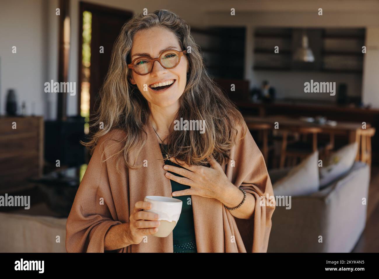 Beautiful senior woman smiling at the camera while standing with a cup of tea in her hand. Cheerful senior woman enjoying a happy retirement at home. Stock Photo