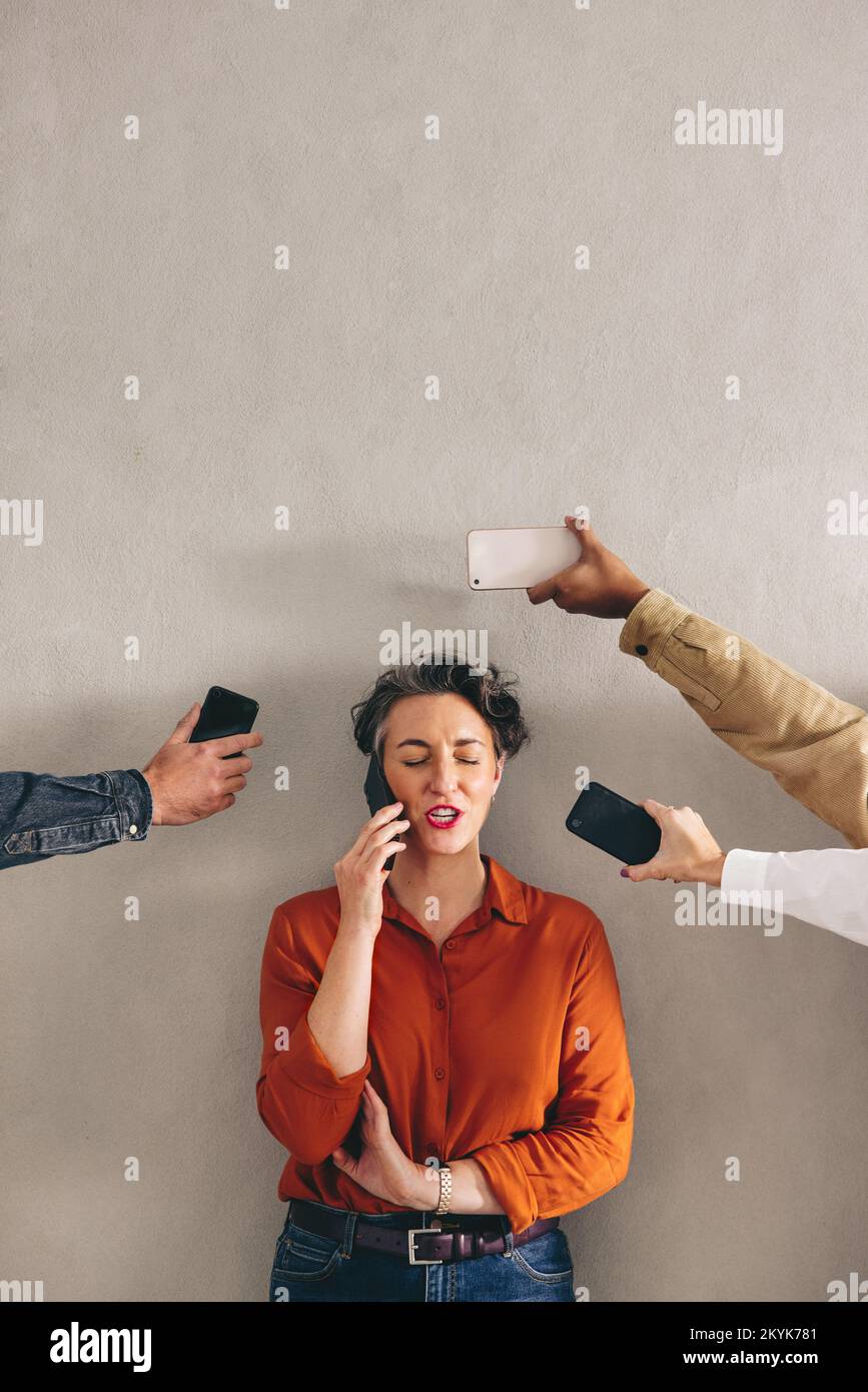 Busy businesswoman speaking on the phone while surrounded by hands holding smartphones. Female business professional answering phone calls in a demand Stock Photo