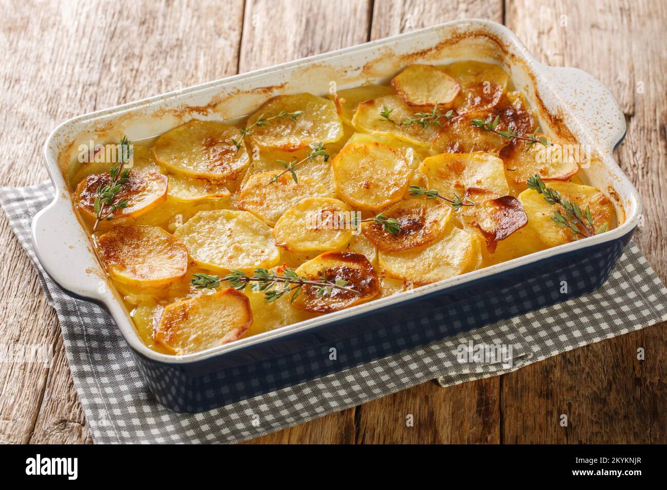 Scalloped potatoes, potato casserole with the addition of herbs, onion and garlic in a ceramic baking dish closeup on the table. Horizontal Stock Photo