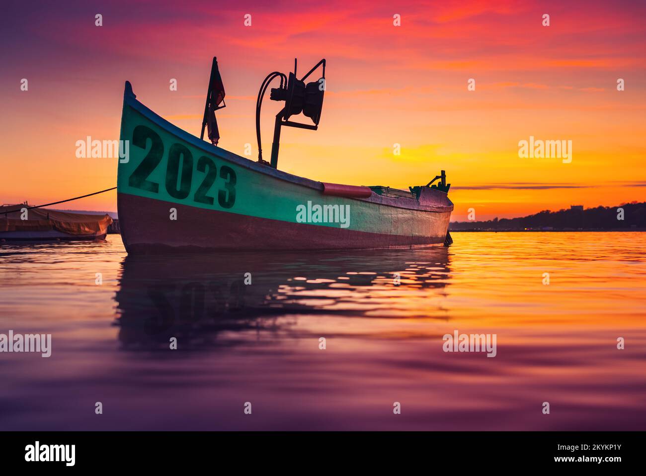 2023 new year concept. Fishing boat on shore and ripple sea water on dramatic colorful sunset Stock Photo