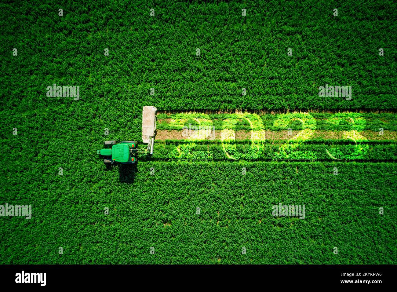 2023 Happy New Year agriculture concept. Red agricultural tractor mowing green field, aerial view Stock Photo