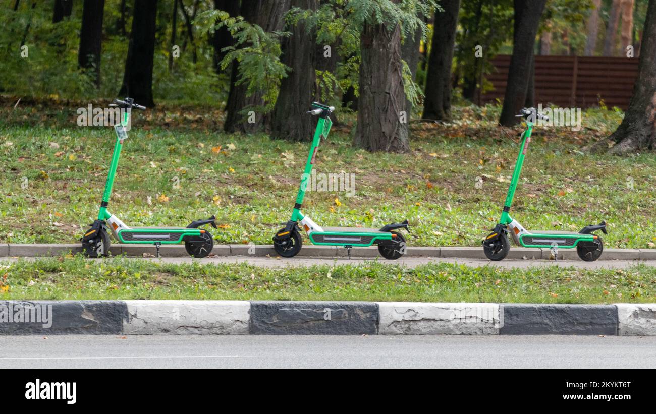 Green Electric Scooters rental standing in city street in greenery