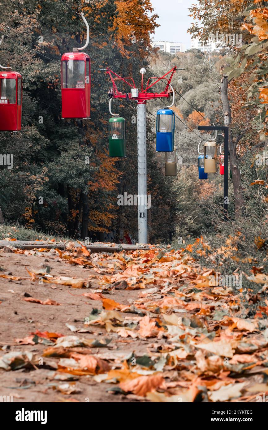 Cableway transport cabins in Kharkiv city recreation park with walking path covered in autumn leaves. Color graded Stock Photo