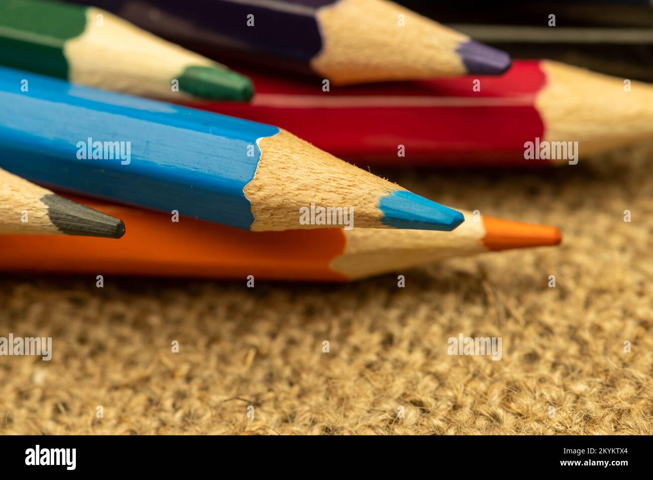 Several colored pencils of different colors on a background of coarse burlap. Close-up, selective focus Stock Photo