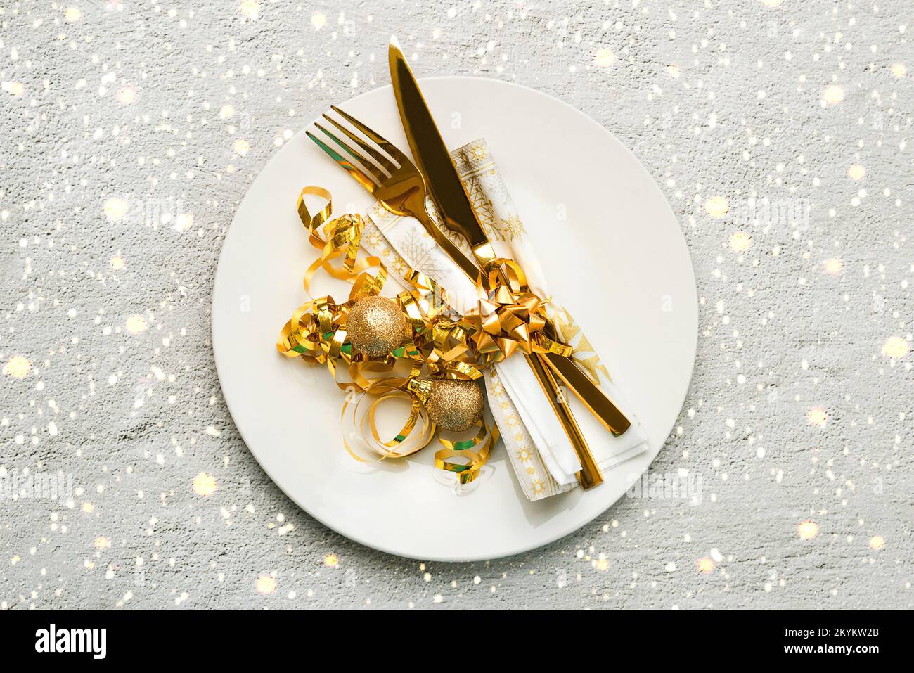 Christmas dinner concept. Top view of golden cutlery on a plate with snowflakes and christmas lights over black background Stock Photo