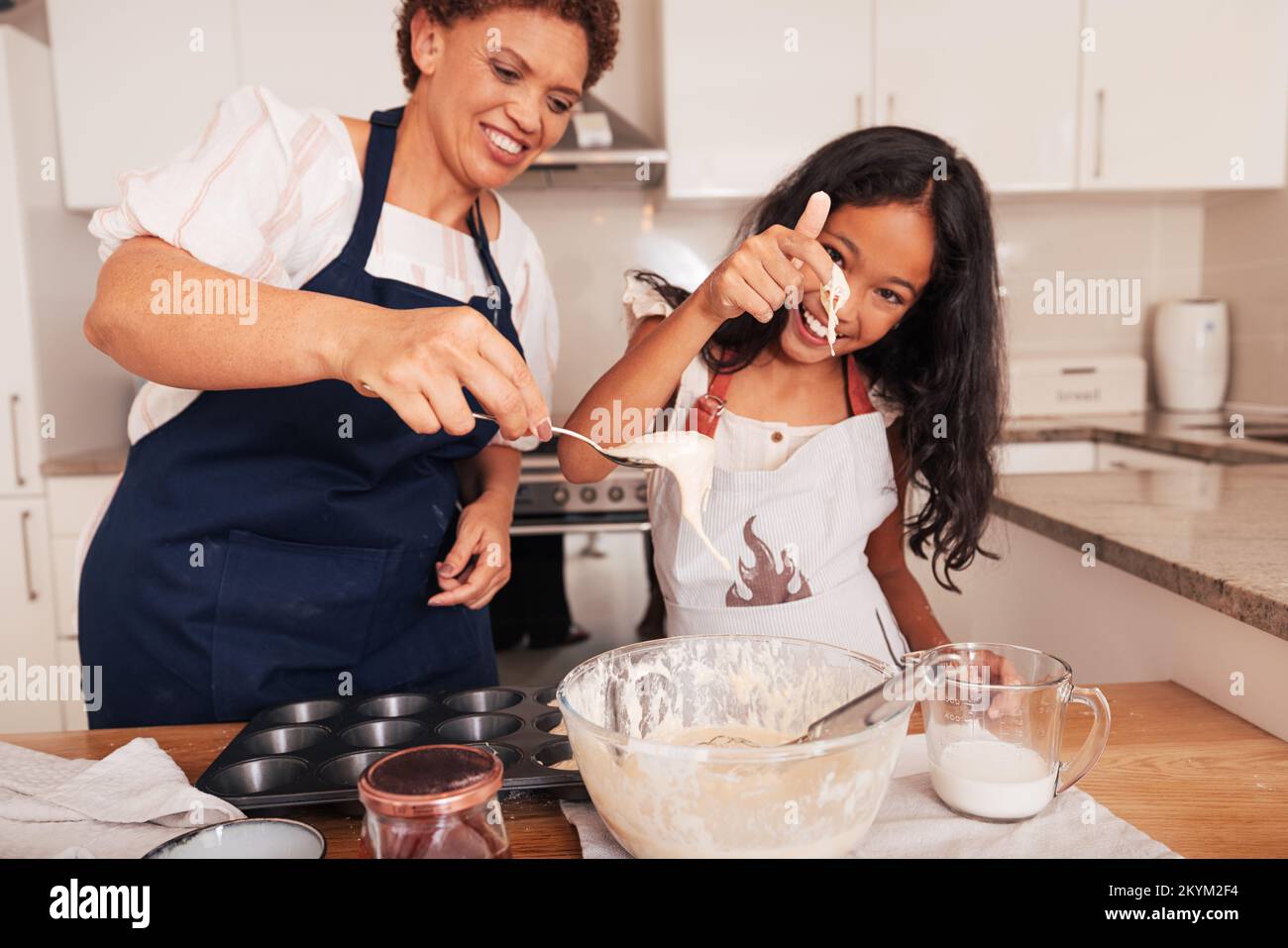 Grandma scoops batter from a bowl with a spoon while granddaughter tests it with her finger Stock Photo