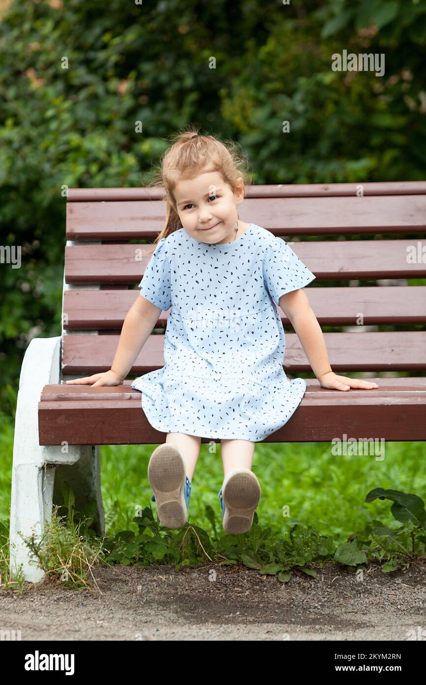Smiling girl sitting on the edge of a wooden bench in the park Stock ...