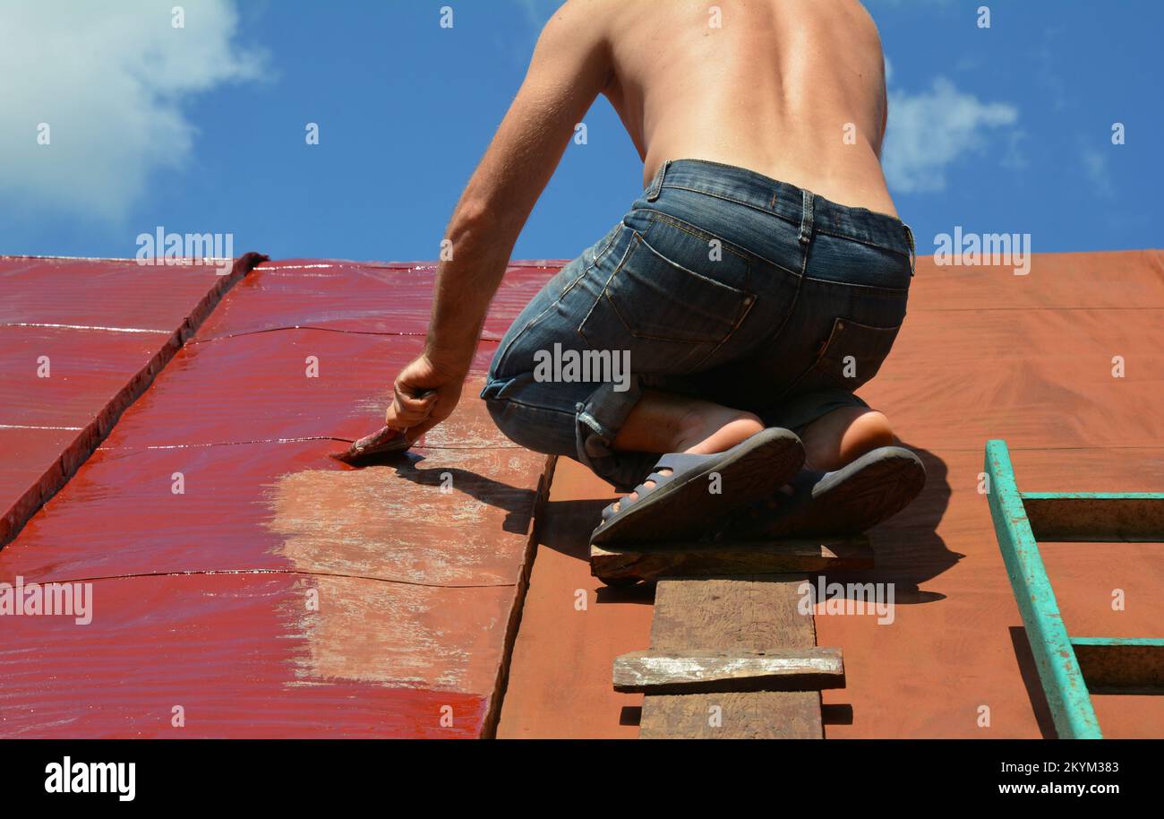 Painting old metal roof with a paint brush. Worker repainting house