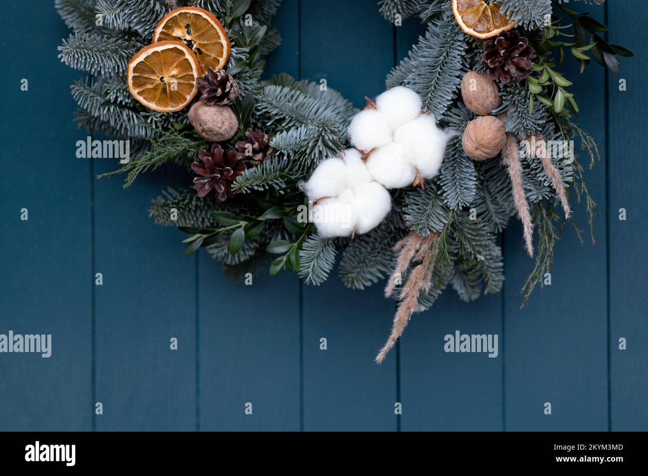 Part of Christmas wreath with pine branches, pine cones, nuts on blue door background with space for text Stock Photo
