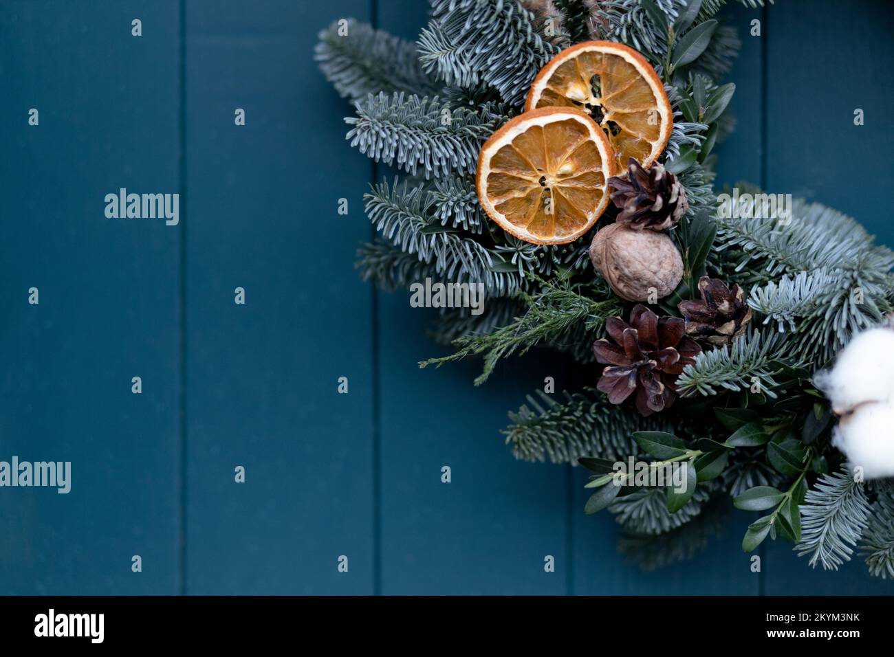 Part of a Christmas wreath consisting of a Christmas tree decorated with pine cones, dried orange on the background of a wooden blue door with space Stock Photo