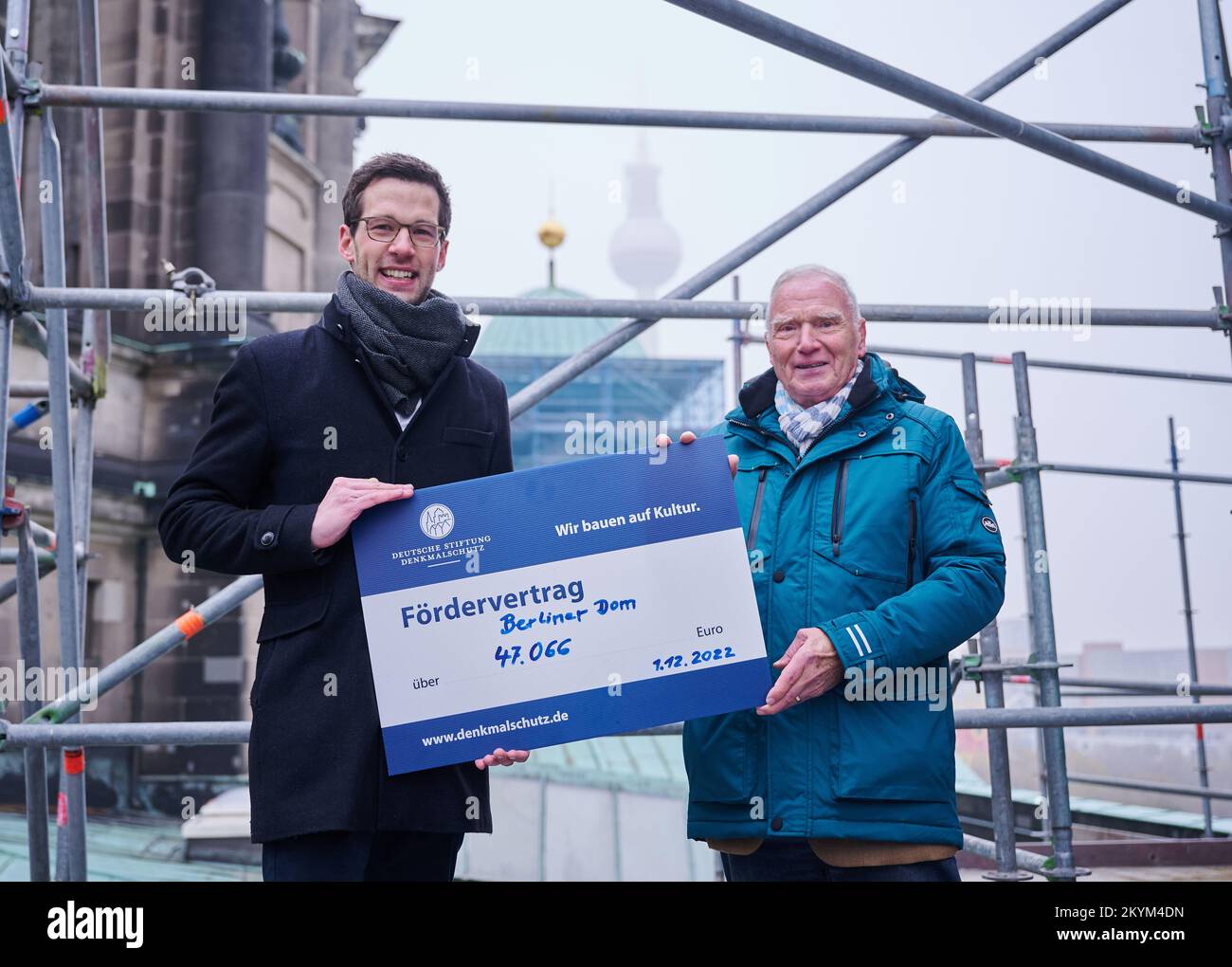 01 December 2022, Berlin: Jan Kingreen (l), managing director of the Berlin Cathedral, and Wolfgang Degen, Deutsche Stiftung Denkmalschutz (German Foundation for Monument Protection), symbolically hold a sign with the funding contract for the Berlin Cathedral in the amount of 47,066 euros while standing on a scaffold of the cathedral. In a nationwide fundraising campaign by the Deutsche Stiftung Denkmalschutz (German Foundation for Monument Protection), 332,535 euros flowed into the facade renovation of the corner towers. Three of the four towers of the church have been freed from a black crus Stock Photo