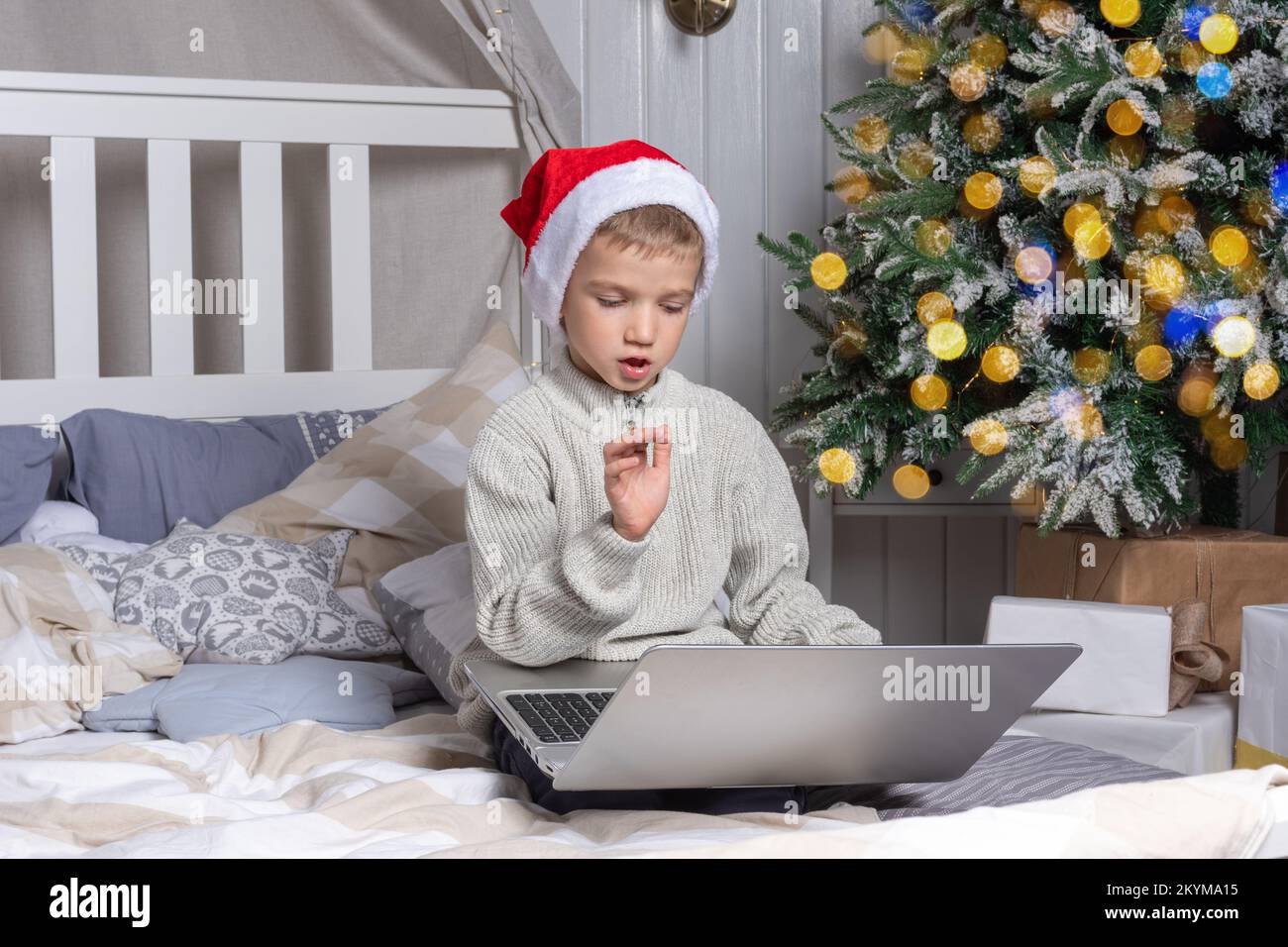 Waiting for a Christmas miracle. A preschool boy in a santa hat communicates via video link explaining which gift he wants to receive in a room decora Stock Photo