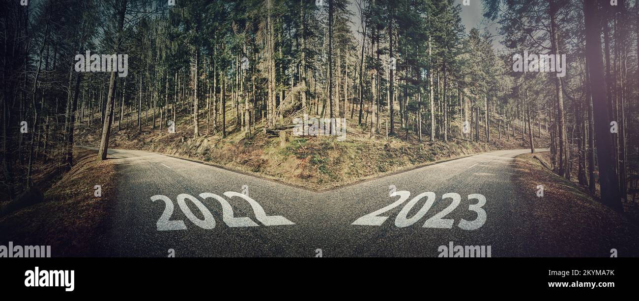 Crossroad scene of 2022 and 2023 years. Asphalt road through the forest splits in two directions,  left and right, choose your way. Different courses, Stock Photo