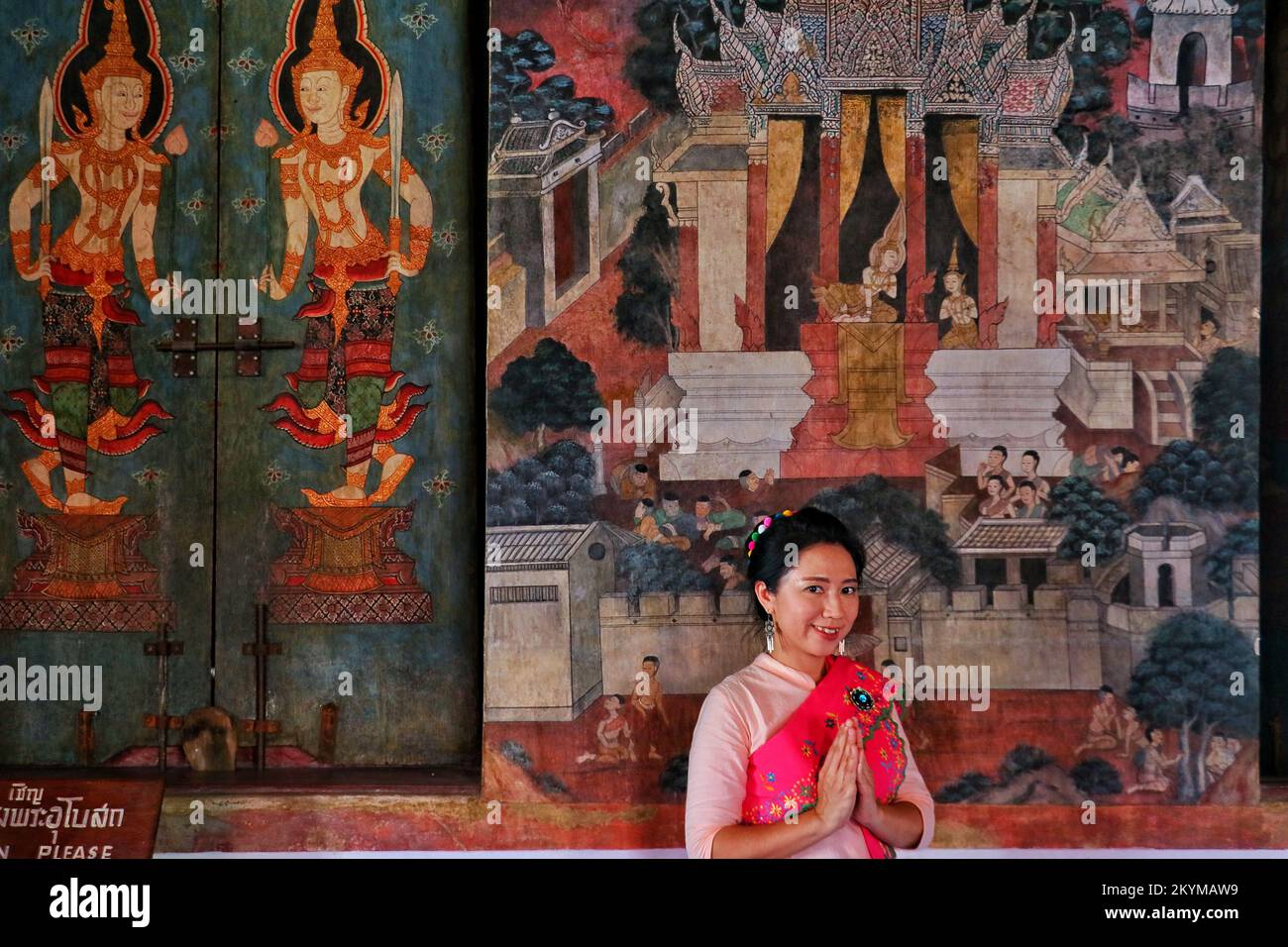 A Thai lady in Mon costume smiles and put hands together in salute at the mural wall of temple Stock Photo