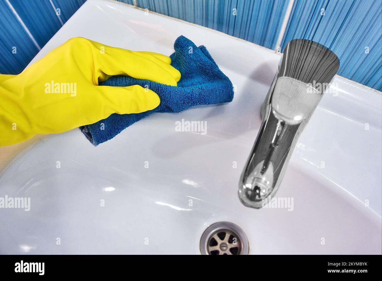 Hand in yellow rubber glove with rag wipes white sink. Cleaning and disinfection with cleaning agent. Clean and shiny sink in toilet.. Stock Photo