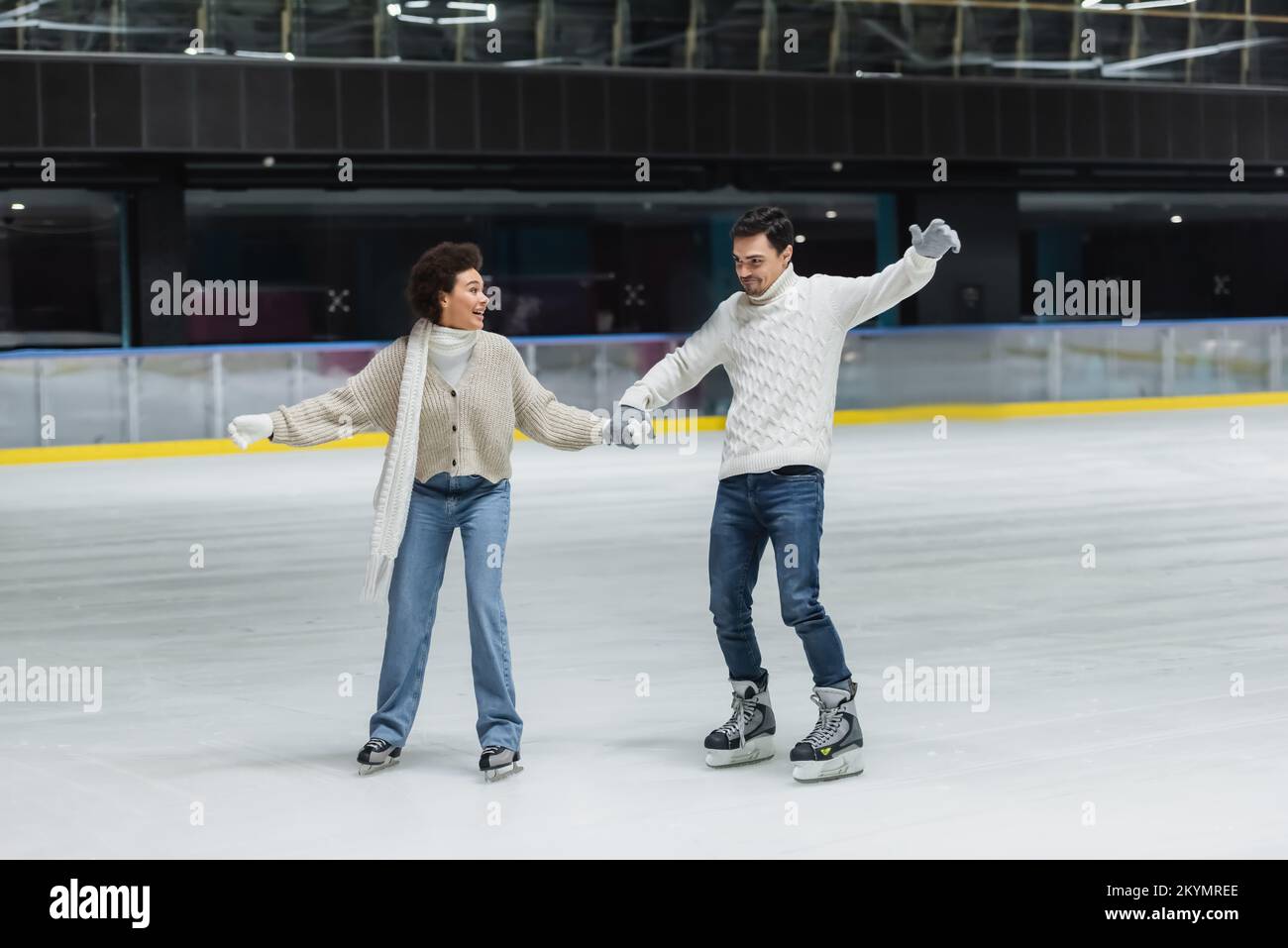 Positive multiethnic couple in gloves ice skating and having fun on rink Stock Photo Alamy