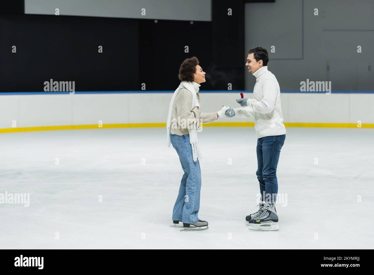 Side view of man doing propose to african american girlfriend on ice rink Stock Photo