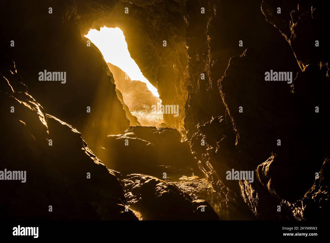 Surf and setting sunlight shining through Merlin's Cave at Tintagel