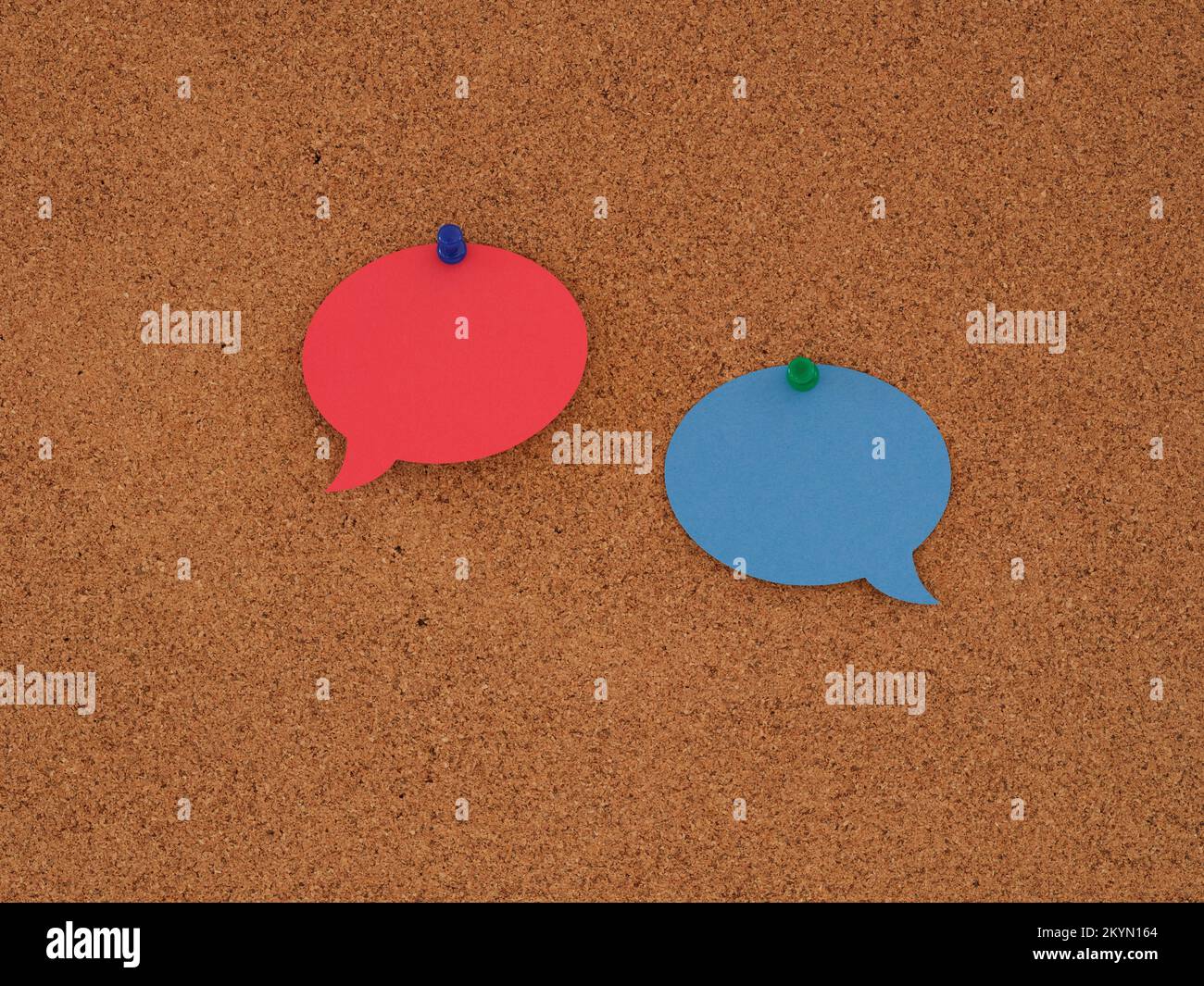 A blank red speech bubble and a blank blue speech bubble pinned to a corkboard. Close up. Stock Photo