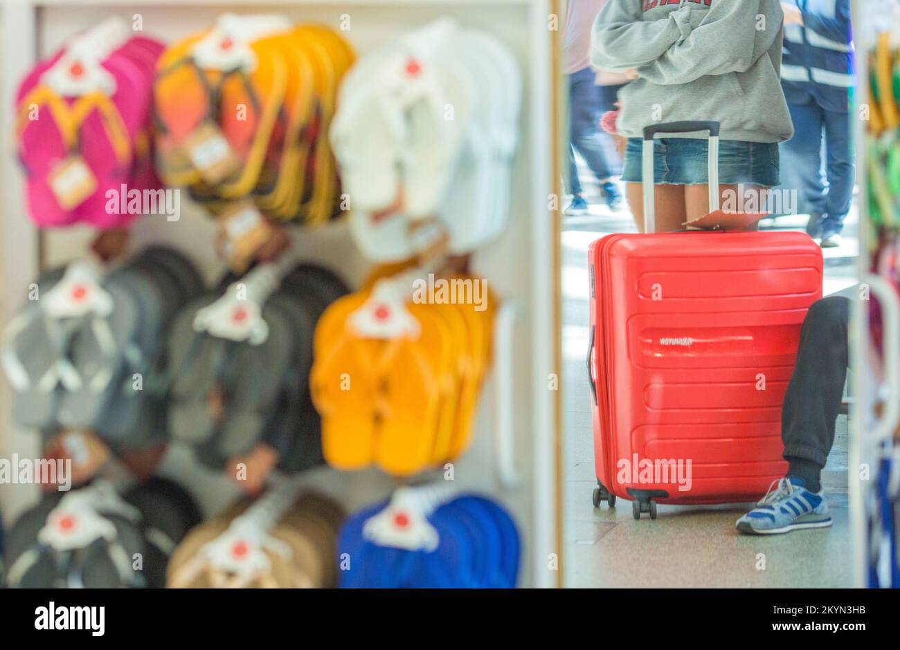 A traveller with a suitcase is reflected in a mirror at a beach sandals shop in St Pancras Station, central London. Stock Photo