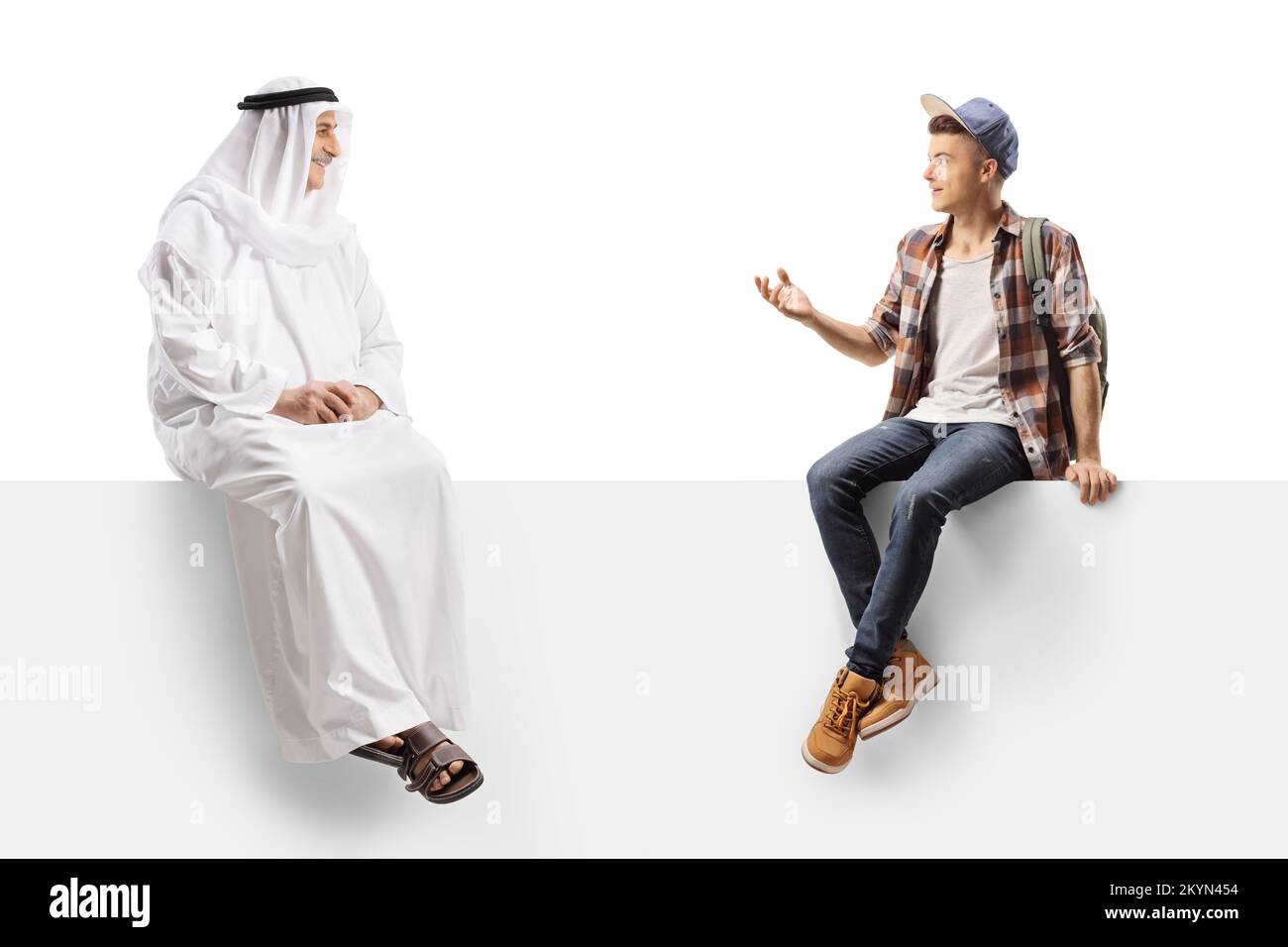 Male student sitting on a white panel and talking to a mature arab man wearing ethnic clothing isolated on white background Stock Photo