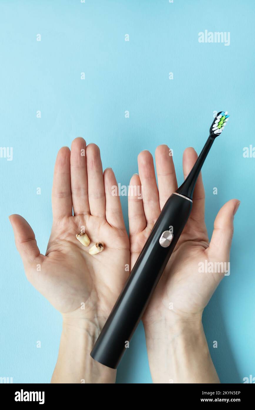 A modern electric toothbrush in one hand and pulled teeth in the other hand on a blue background. Tooth extraction operation. The concept of hygiene f Stock Photo