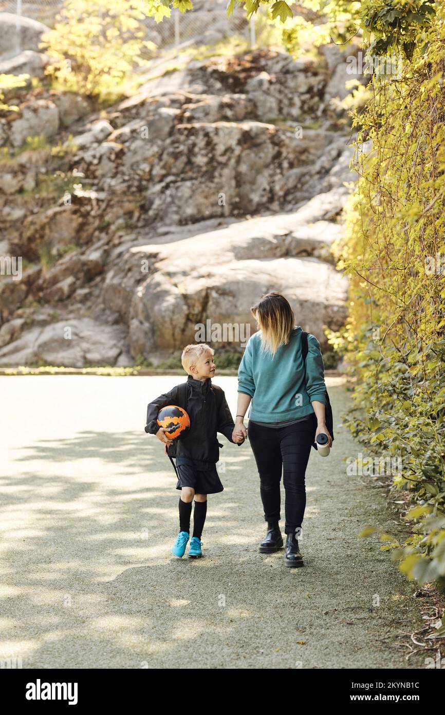 Woman talking and walking with son holding soccer ball in ground Stock Photo