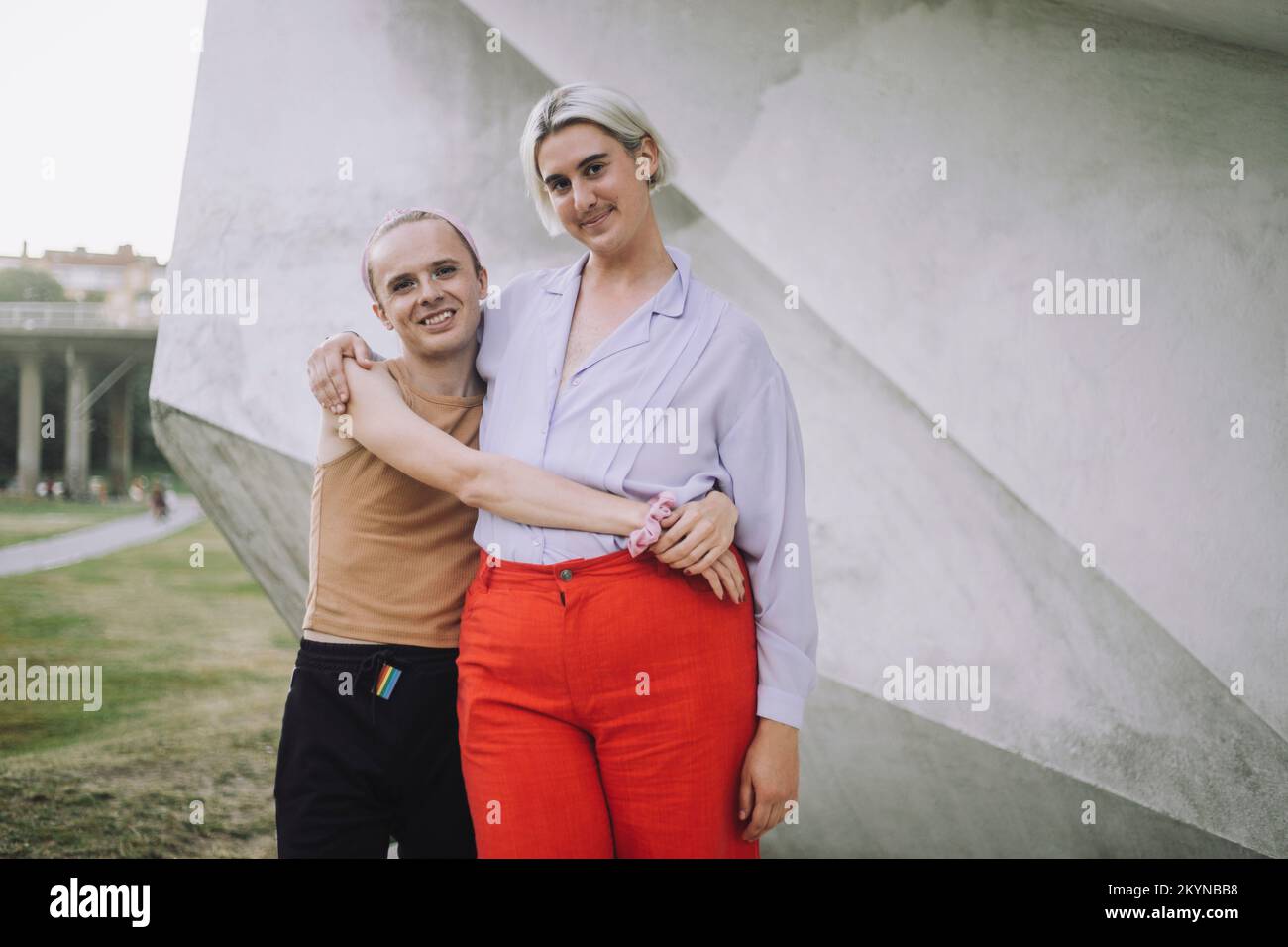 Portrait of smiling non-binary friends standing against wall at park Stock Photo