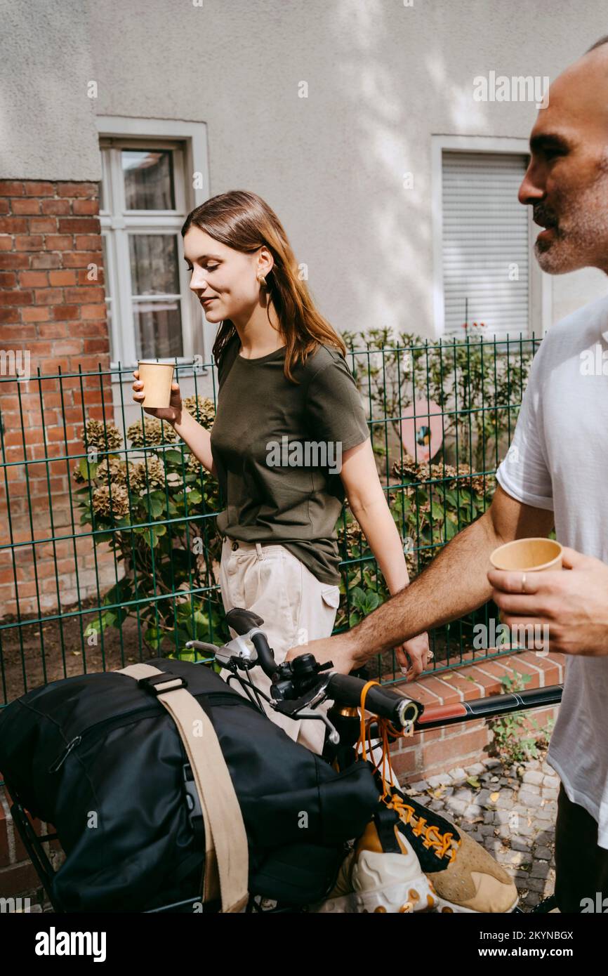 Young woman with male friend wheeling with bicycle while having coffee Stock Photo