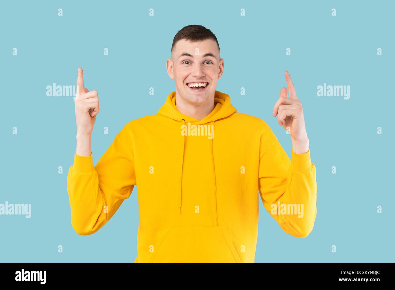 Look up. Happy caucasian guy pointing fingers upward, showing something over blue background, studio shot Stock Photo