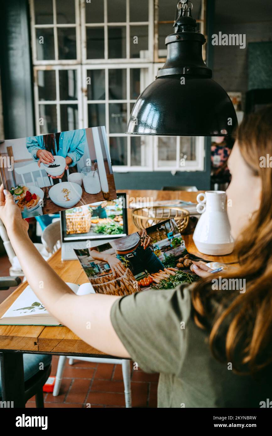 Young food stylist looking at photographs while working in studio Stock Photo