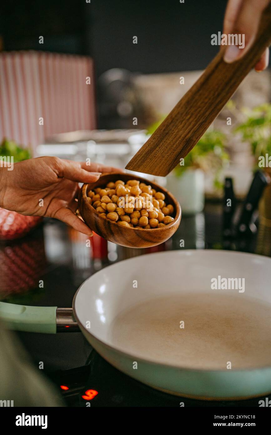 Using Cooking Spoon Hands of female chef adding chickpea in cooking pan using wooden spoon ...