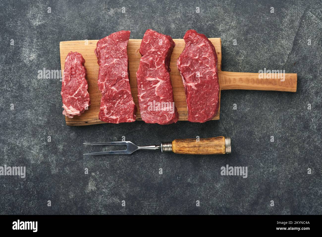 Raw steaks. Top blade steaks on wood burning board with spices, rosemary, vegetables and ingredients for cooking on black background. Top view. Copy s Stock Photo