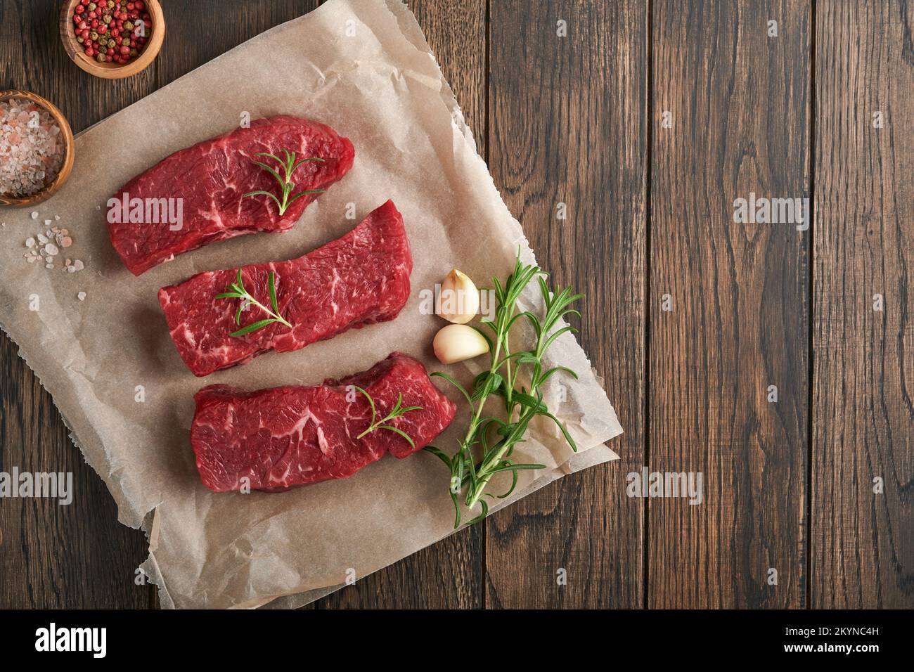 Raw steaks. Top blade steaks on wood burning board with spices, rosemary, vegetables and ingredients for cooking on old wooden background. Top view. C Stock Photo