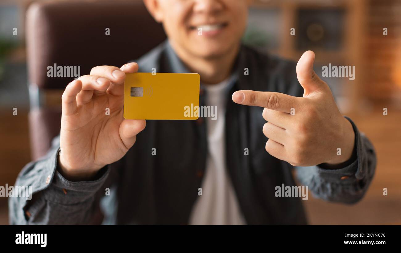 Glad middle aged asian man pointing finger at credit card in home office interior, cropped Stock Photo