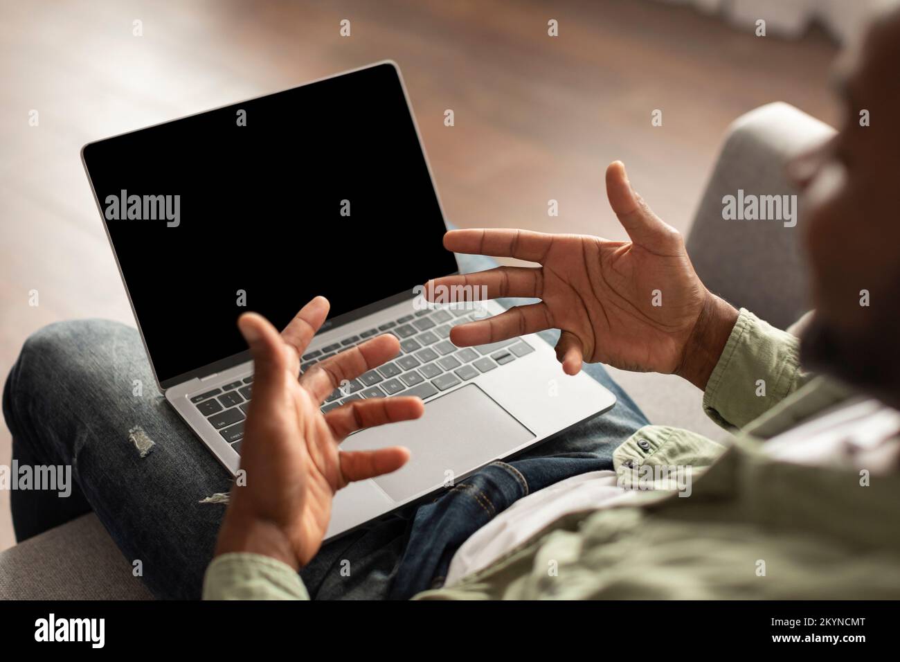 Adult african american guy sit on sofa watch video on laptop with blank screen, gesturing has online call Stock Photo