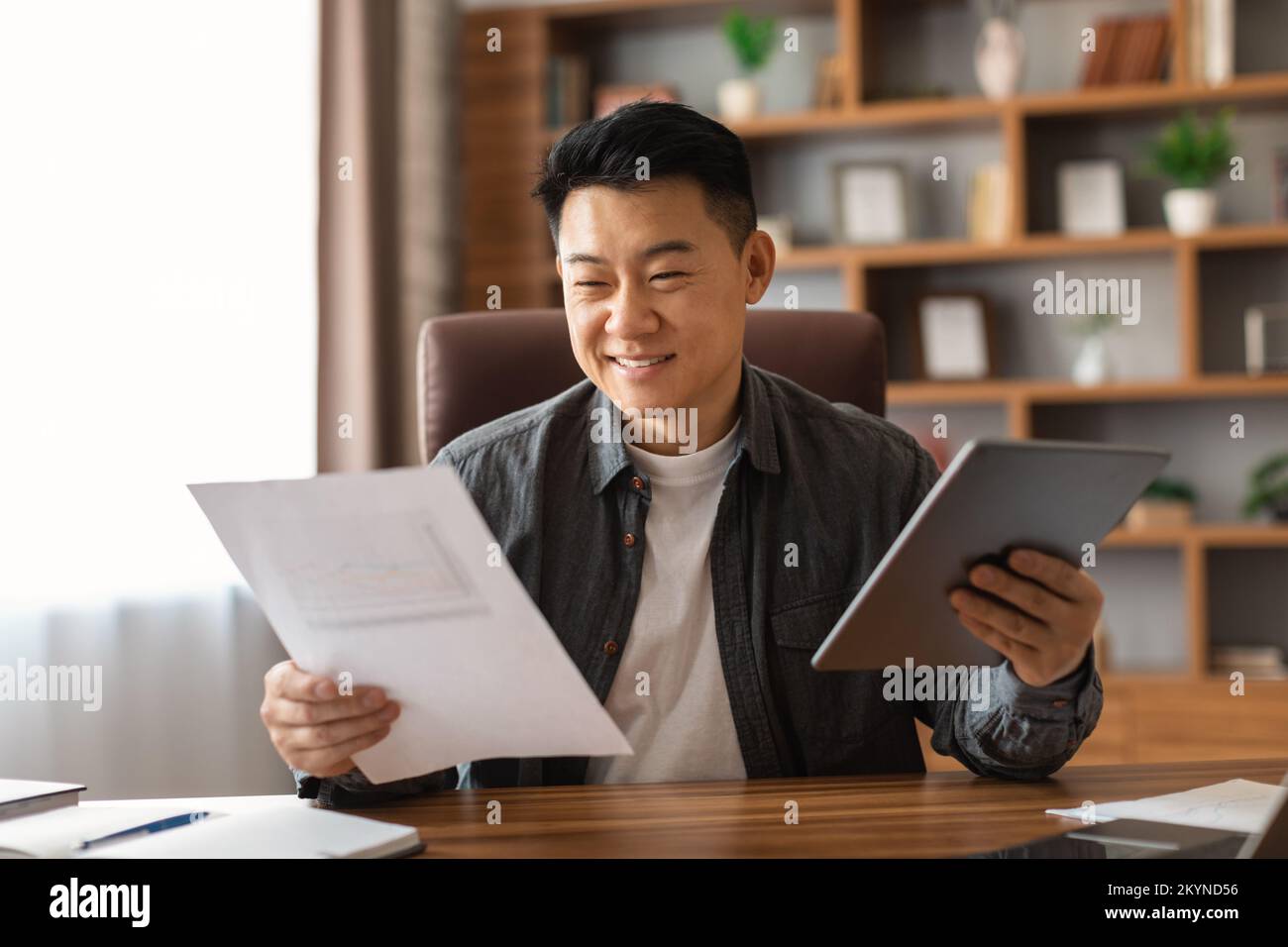 Cheerful middle aged japanese ceo businessman with documents and tablet works in home office interior Stock Photo
